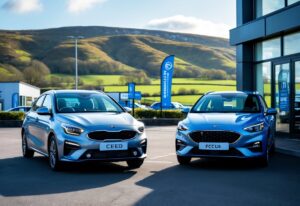 Two compact cars parked side by side outdoors at a car dealership with green hills in the background.